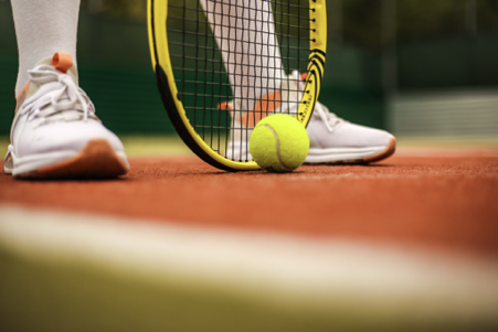 A close-up image of a tennis racket positioned next to a vibrant yellow tennis ball.